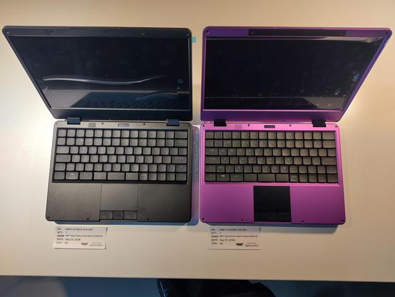 a black hyper reform next and a purple hyper reform next on a white table surface, shot from above. the displays still have protective foil on them.