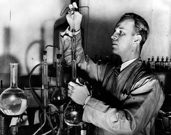 Black & White flash photo of Ray Pinker, young (he still has his hair) working in a chemist lab.